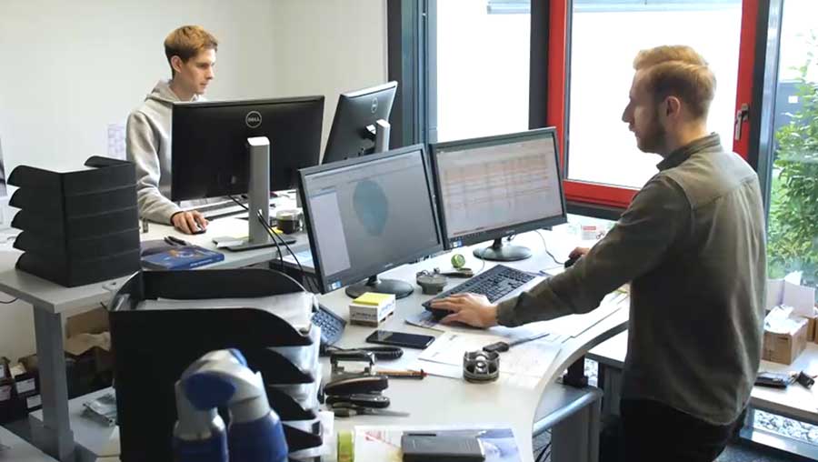 Zwei Männer arbeiten an Computern in einem modernen Büro mit mehreren Monitoren.